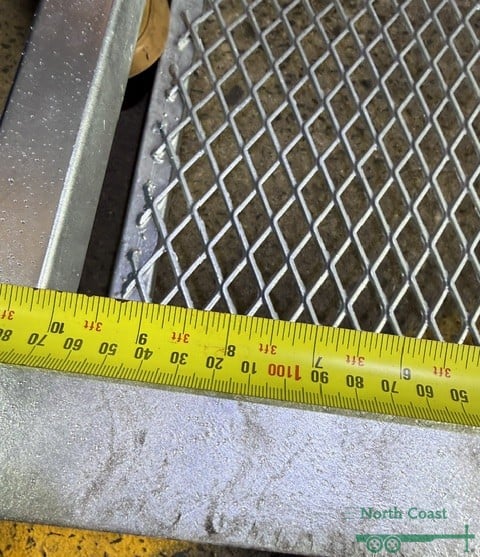 Close-up top view of a hot-dipped galvanised steel mower pad with a yellow measuring tape showing an internal measurement of 1170mm along the diamond-pattern mesh floor frame