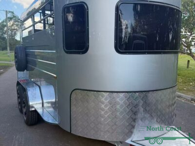 Exterior profile view of a white 2-Horse Straight Load (2HSL) Entry-Level Standard Horse Float, featuring a full aluminium body kit, hot-dipped galvanised chassis, stylish alloy wheels, a gas-strut assisted rear loading ramp, an open side design with safety bars, and an offset pedestrian door.