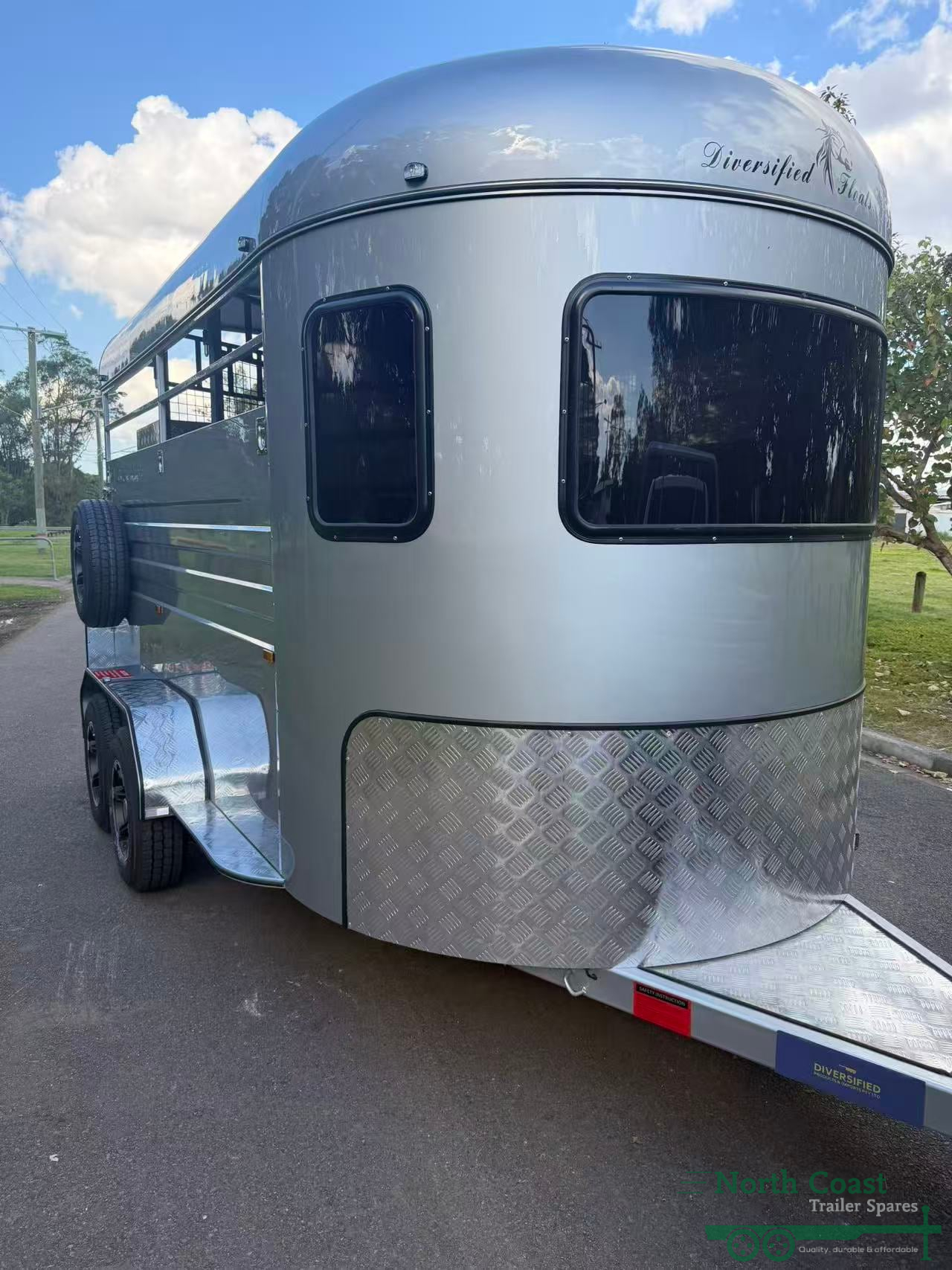 Exterior profile view of a white 2-Horse Straight Load (2HSL) Entry-Level Standard Horse Float, featuring a full aluminium body kit, hot-dipped galvanised chassis, stylish alloy wheels, a gas-strut assisted rear loading ramp, an open side design with safety bars, and an offset pedestrian door.